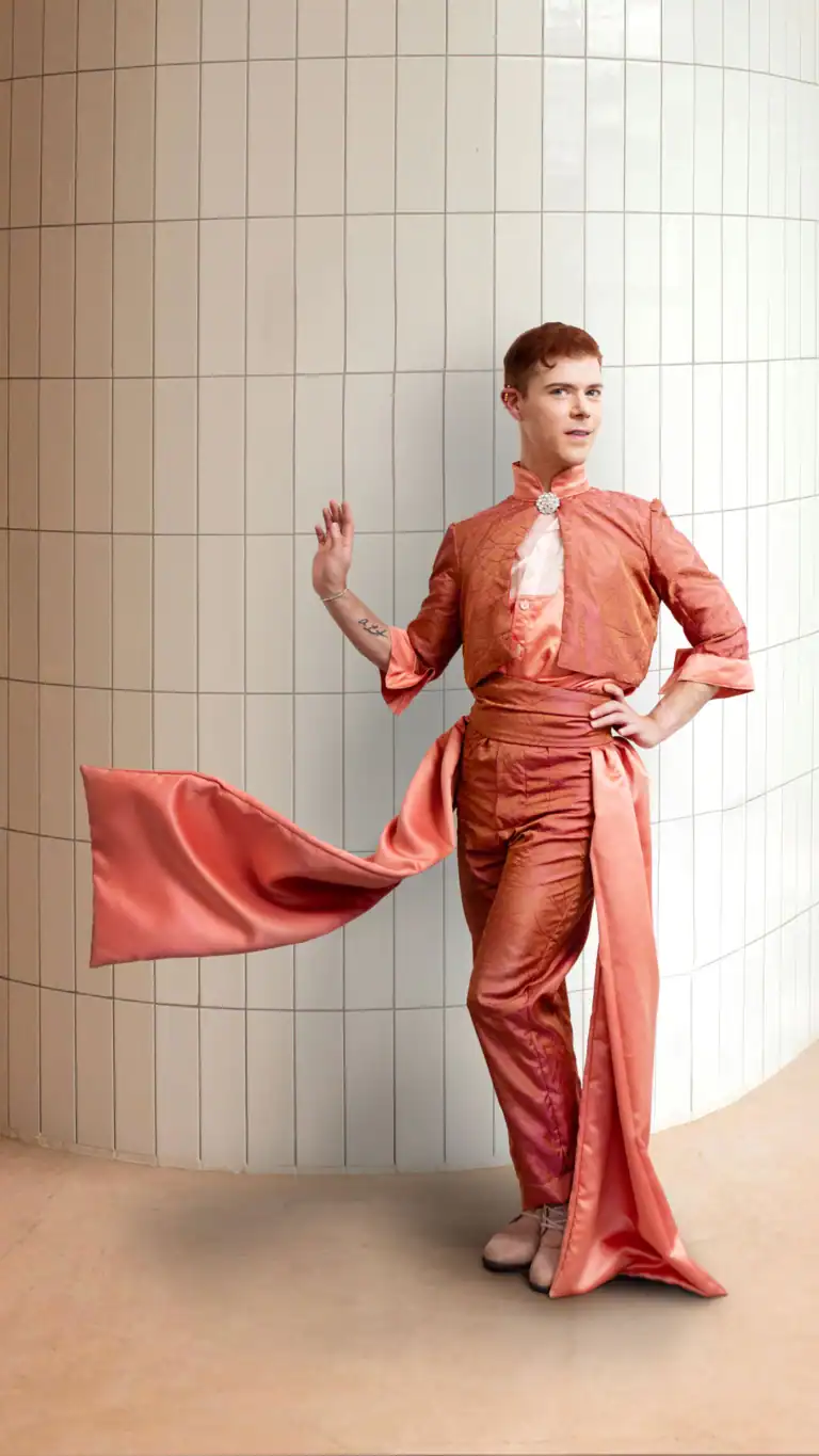 Designs Elijah in a clean white tile room showing his fashion designs with flowing fabrics.